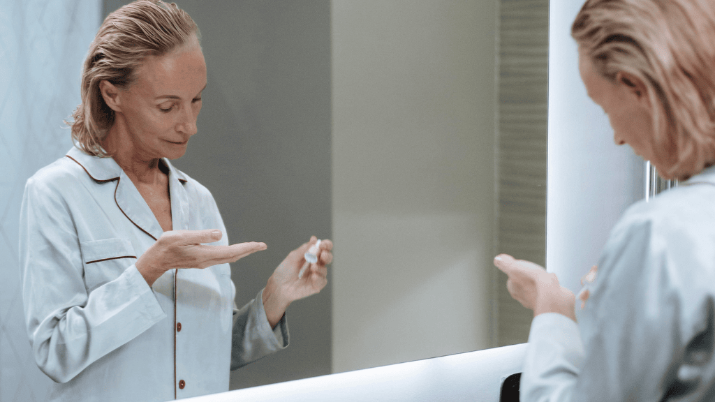 Applying a gentle skincare serum as part of a rosacea-friendly routine in front of a bathroom mirror.